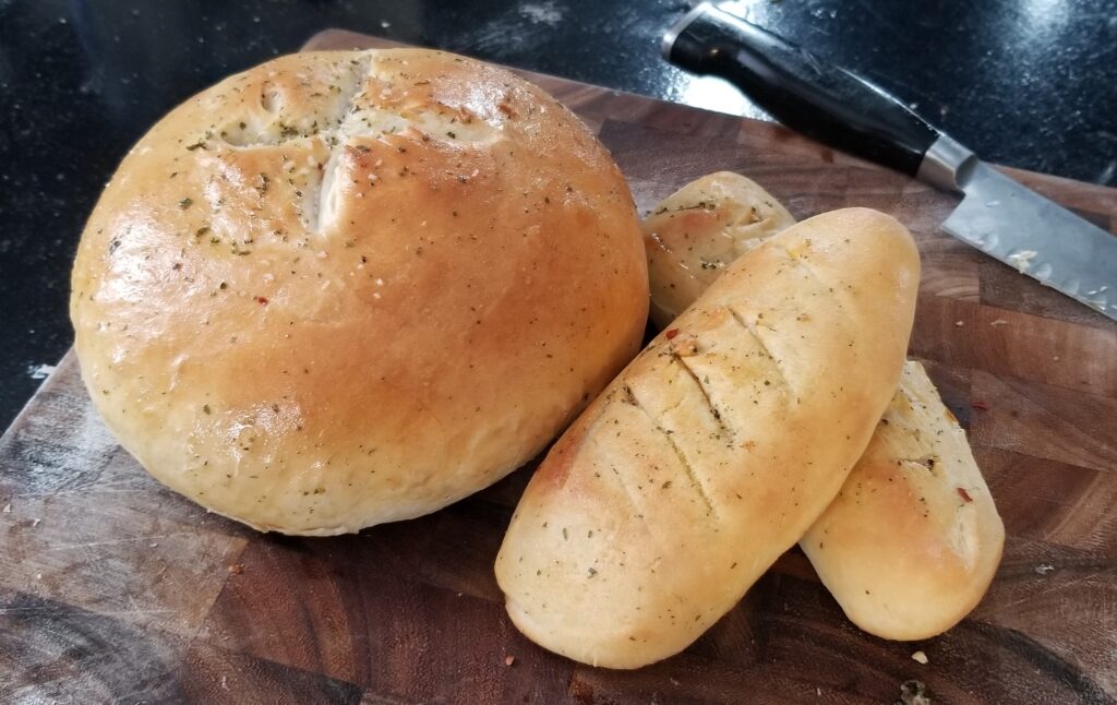 Freshly baked bread loaf and rolls on a wooden cutting board.