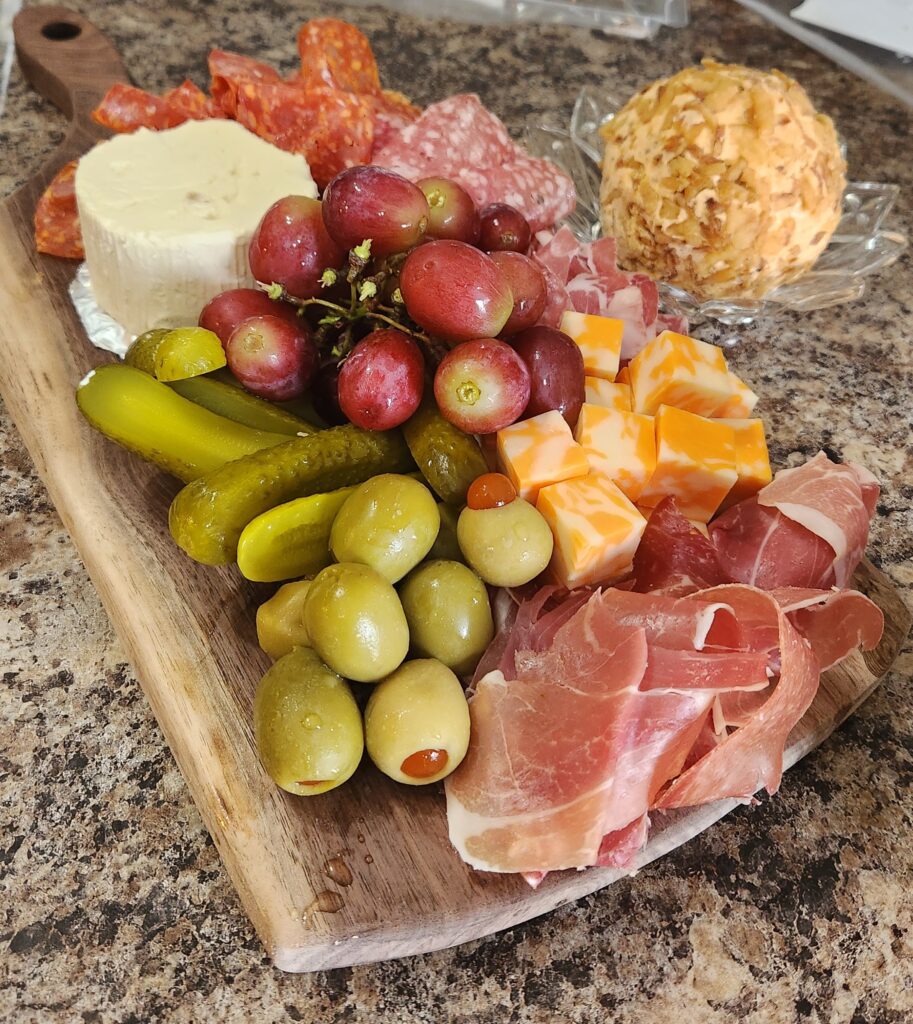A beautifully arranged charcuterie board featuring meats, cheeses, olives, pickles, and grapes.