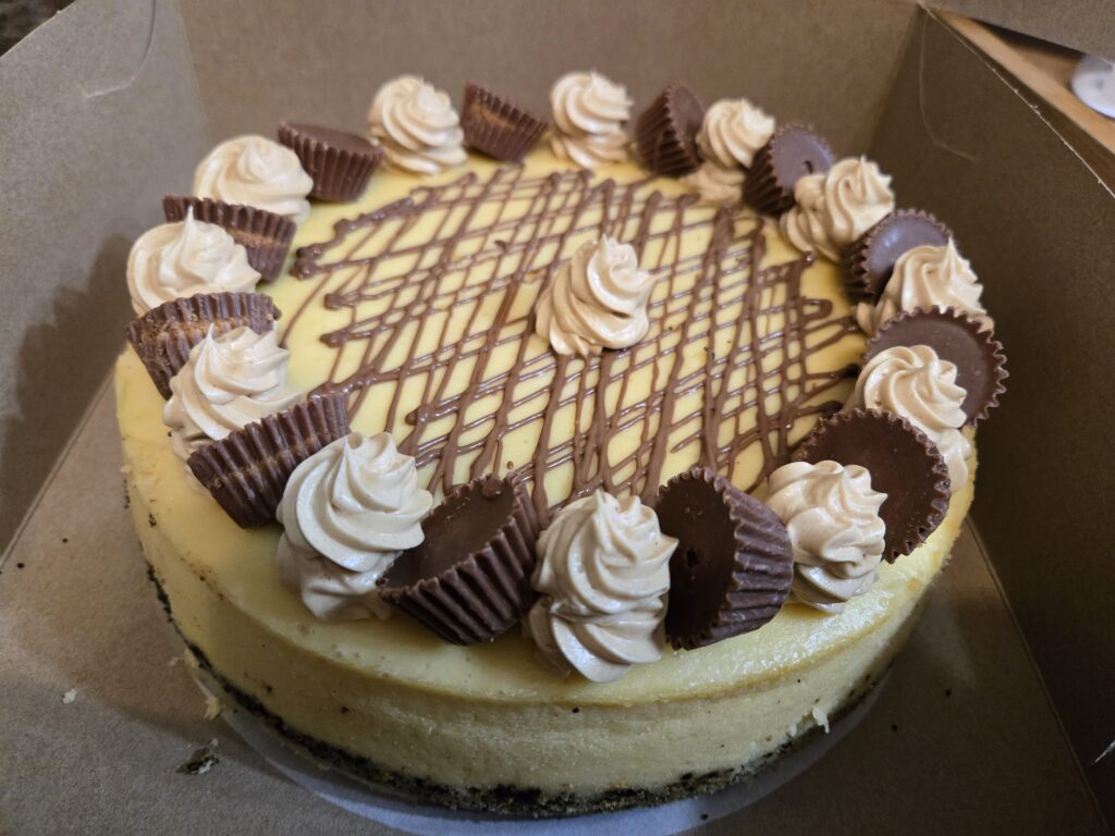 A delicious cheesecake topped with chocolate drizzle and mini peanut butter cups.