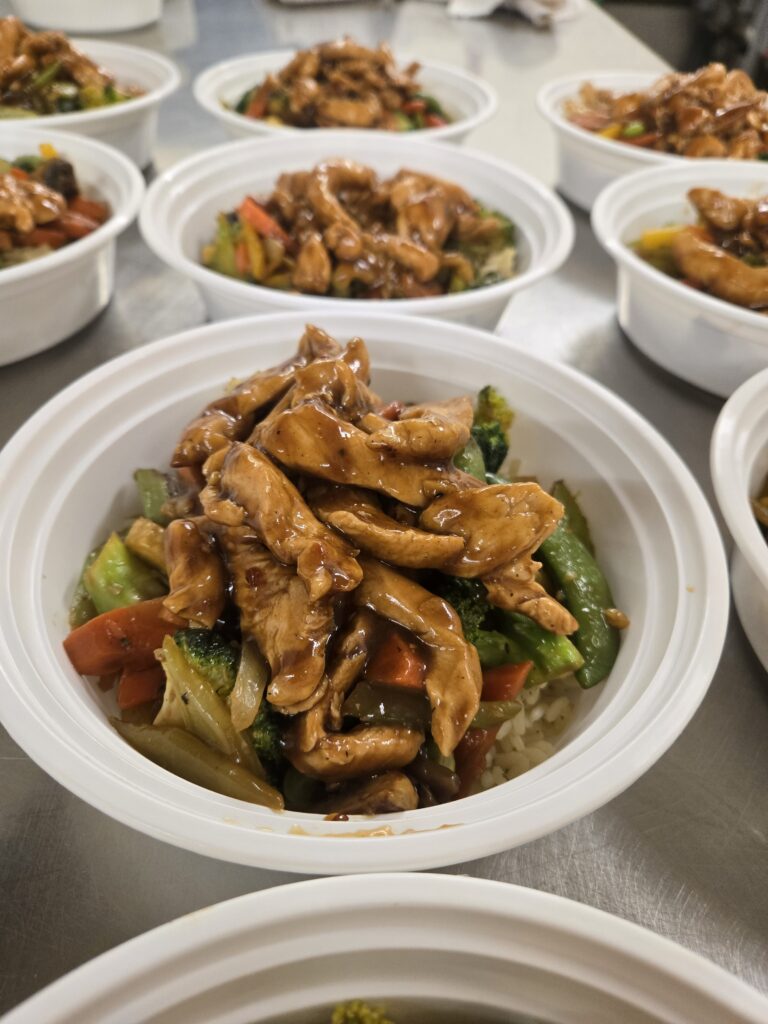 Bowls of stir-fried chicken with vegetables and rice, arranged in a kitchen setting.