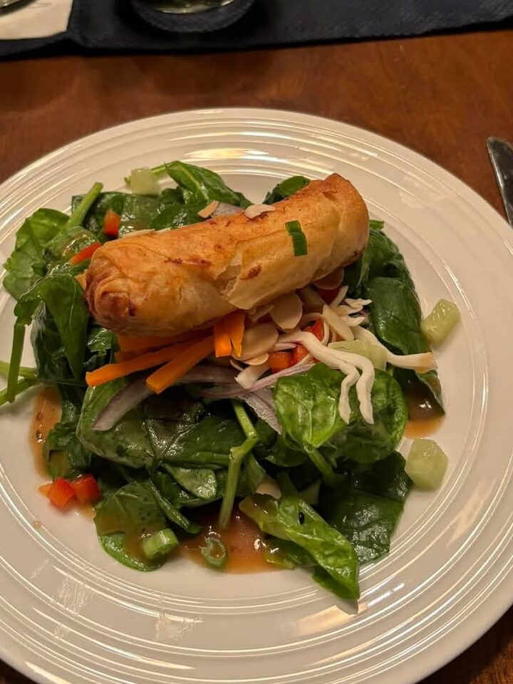 A vibrant salad with spinach, vegetables, and a crispy spring roll on top.