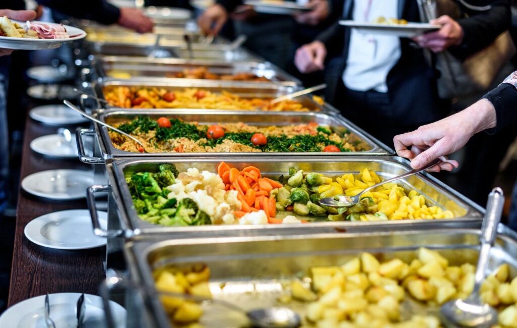 A buffet with various dishes, including vegetables and rice, being served to guests.