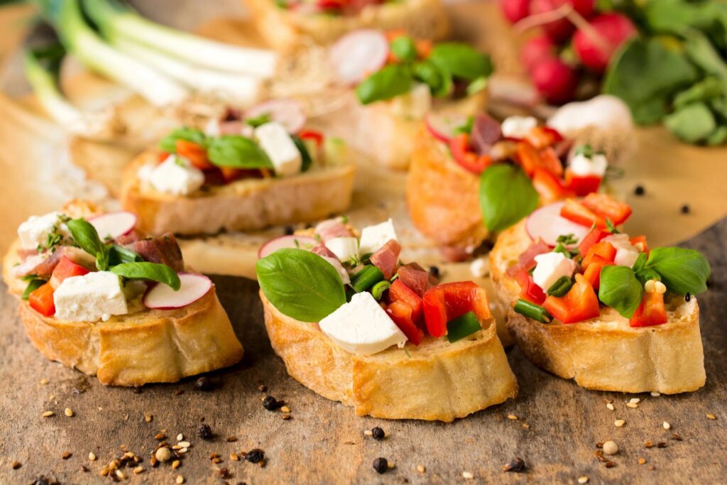 A colorful array of bruschetta topped with vegetables, herbs, and cheese on a wooden surface.